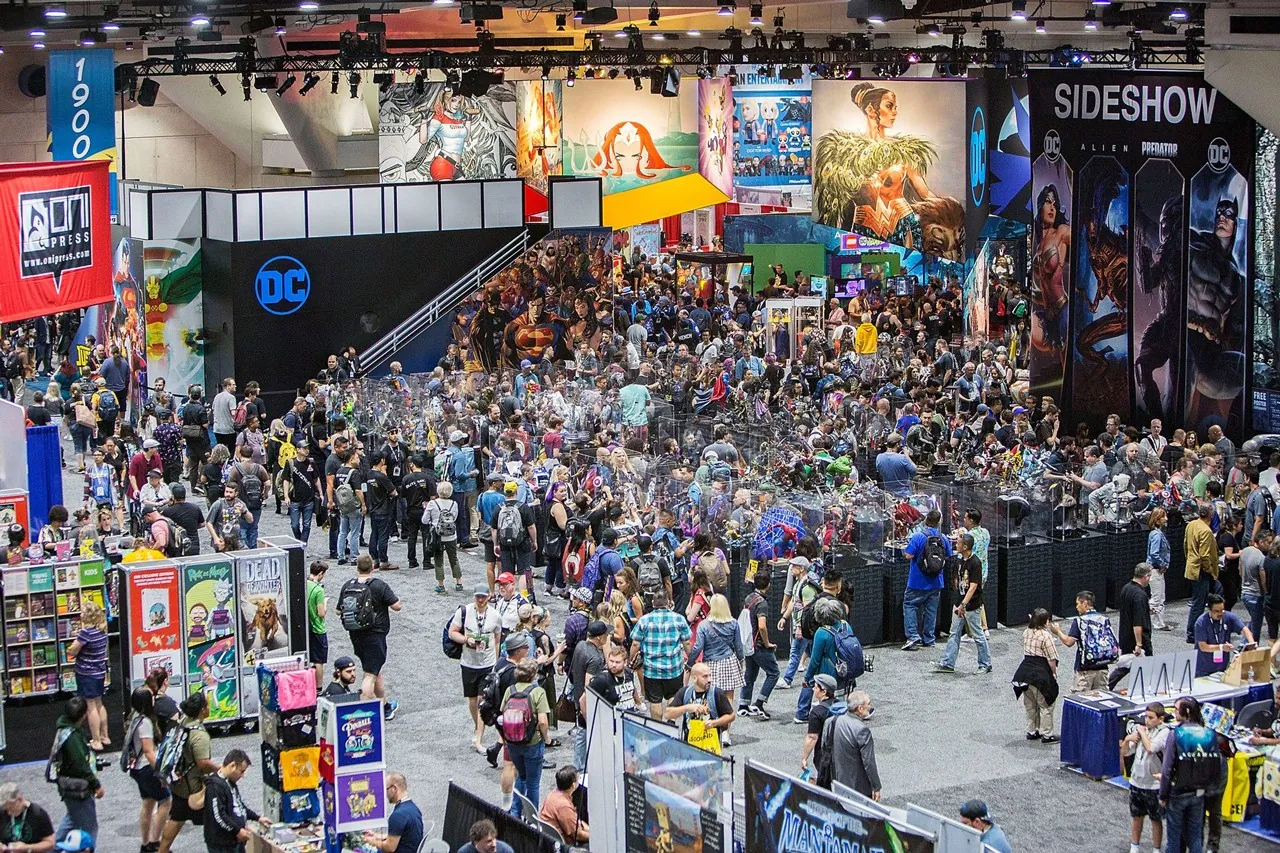 Fans filling the aisles of a busy convention hall lined with exhibitor stands